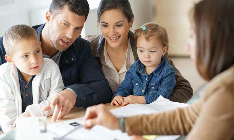 a photo of three adults sitting a table with two children, the adults are looking at papers