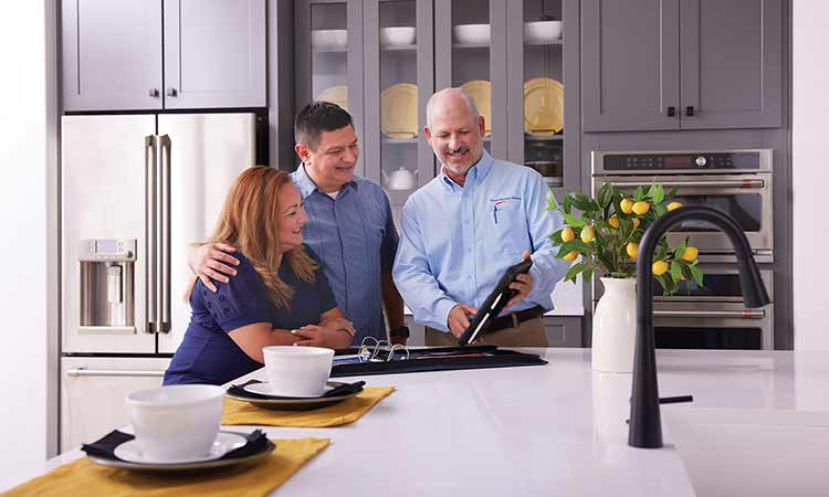 A David Weekley Homes Warranty Service Manager stands in a kitchen with two homeowners, they are all looking at a tablet
