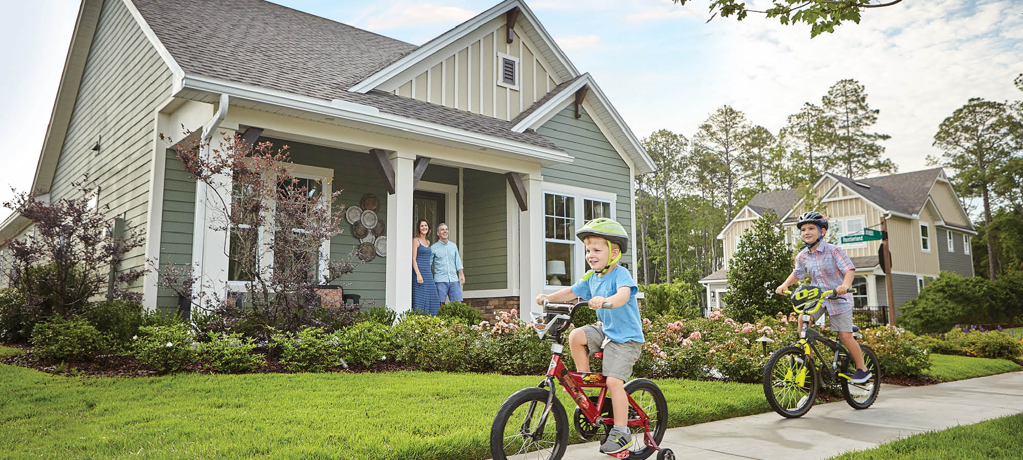 children on a tricycle and bicycle riding on a sidewalk in front of a home