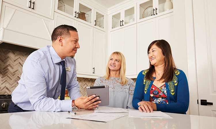 A David Weekley Homes Personal Sales Consultant sits st a kitchen counter with a real estate agent and a homeowner