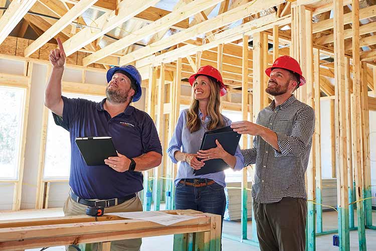 three people wearing hardhats standing in a home under construction