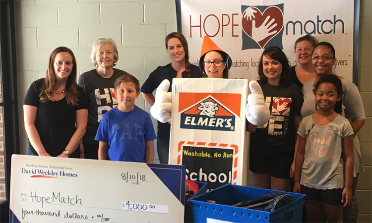 people standing around a large novelty donation check and donated school supplies