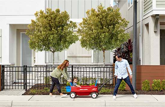 man and woman pulling a child that is sitting in a red wagon down the sidewalk