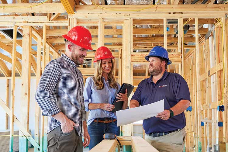 three people wearing hard hats are standing in a home under construction and looking at sheet of paper