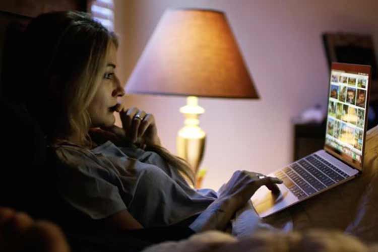 a woman sits up in bed looking at a laptop