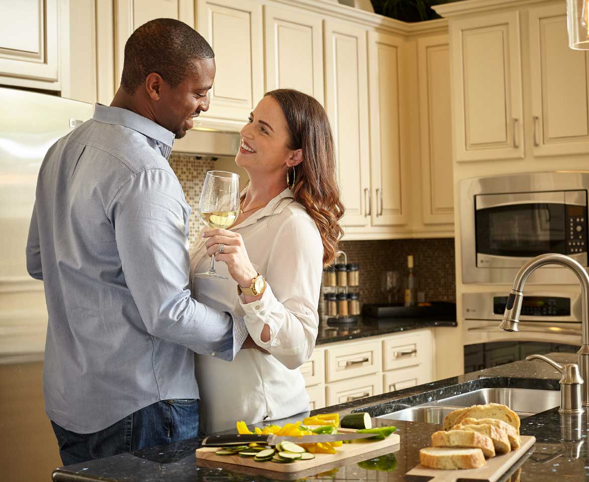 A man and woman standing in a kitchen with glasses of wine