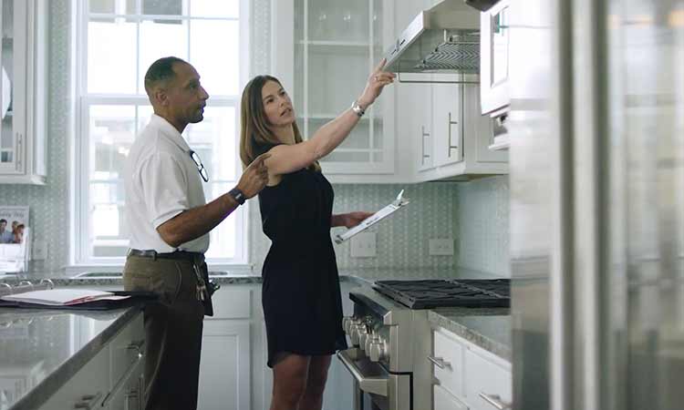 A man and woman stand in a kitchen looking at a vent hood