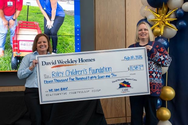 Two women stand holding a large donation check