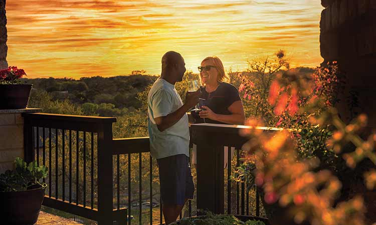 A man and woman stand on a deck during sunset