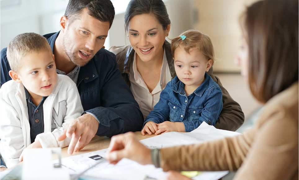 A man and woman sit at a table with another woman holding two children