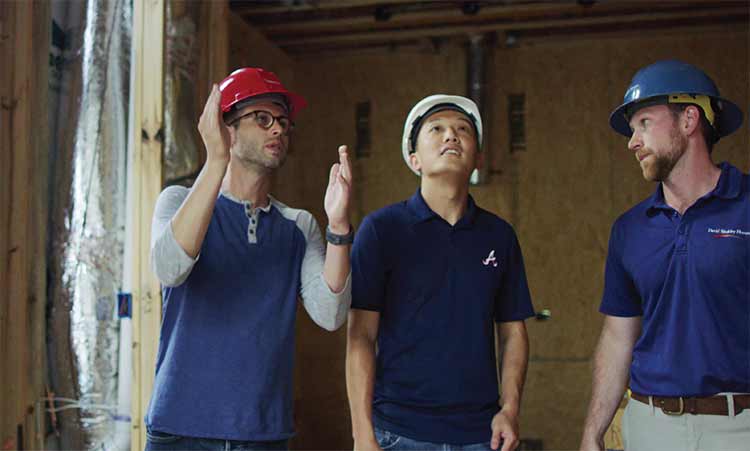 A David Weekley Homes Personal Builder and two Homeowners stand in a home that is under construction, all three people are wearing hard hats