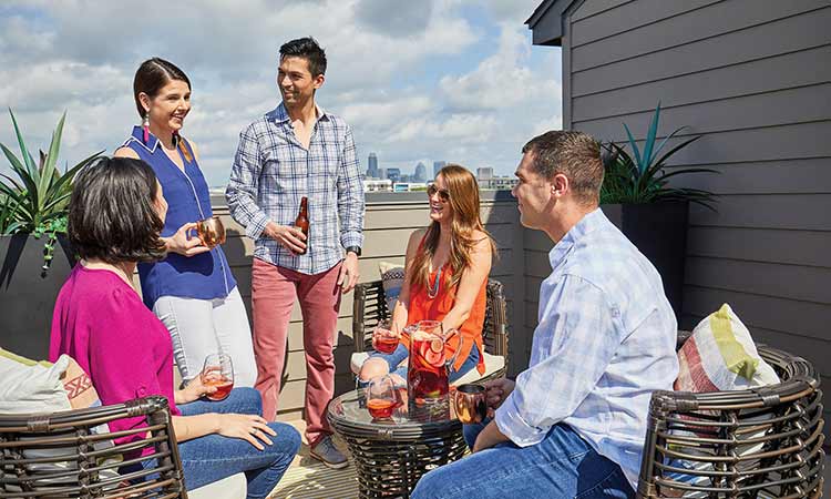 five people sit on a rooftop desk talking and smiling