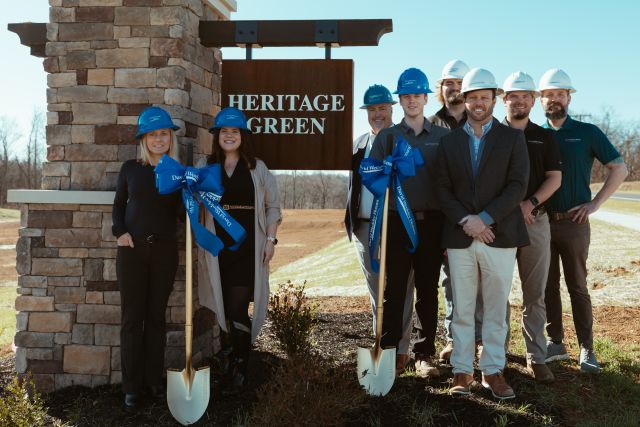 a group of people wearing hard hats stand in front of the Heritage Green sign