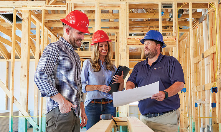 three people stand in a home that is under construction, all three people are wearing hard hats
