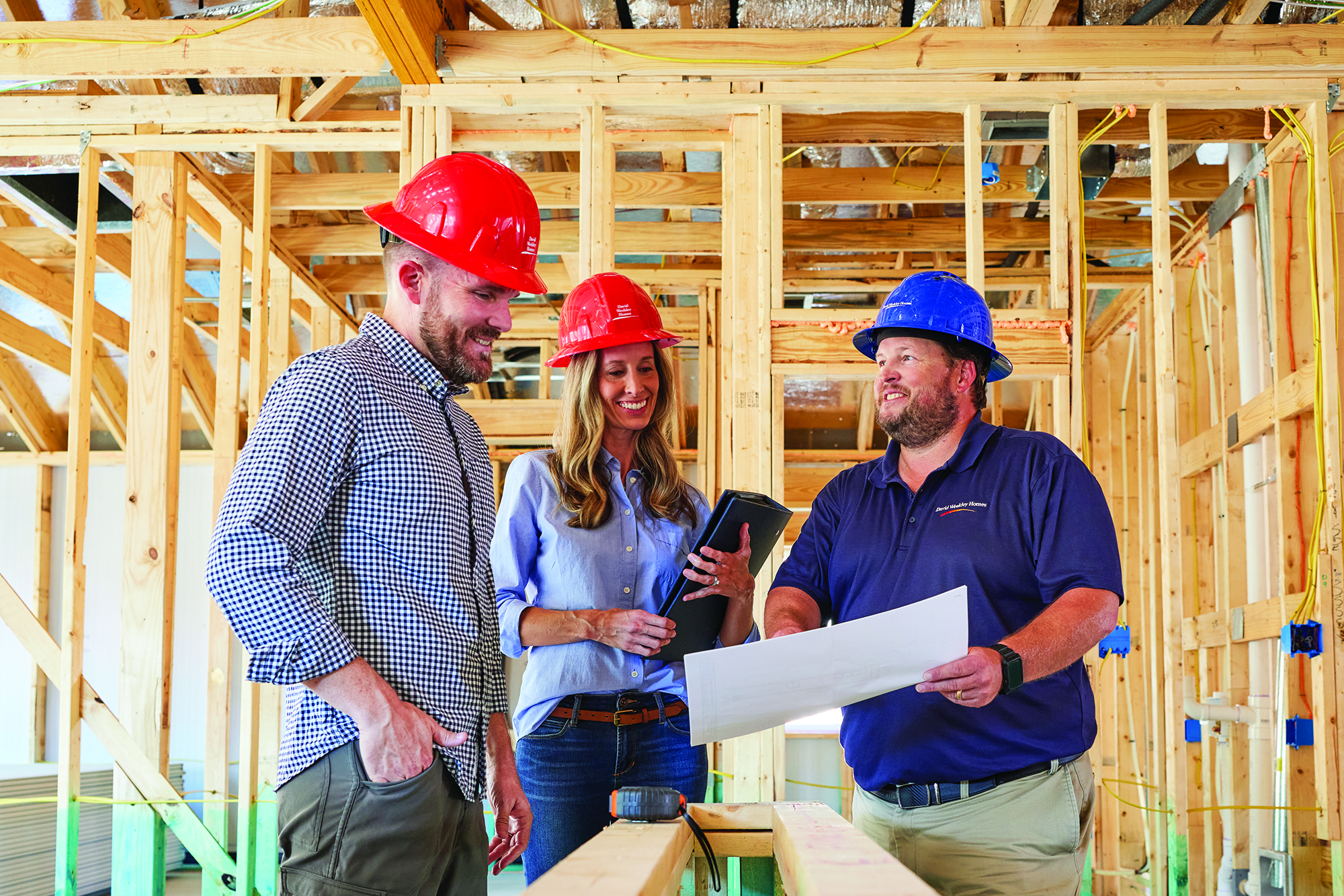 David Weekley Homes Personal Builder standing with customers, all are wearing hardhats, in a home that is under construction