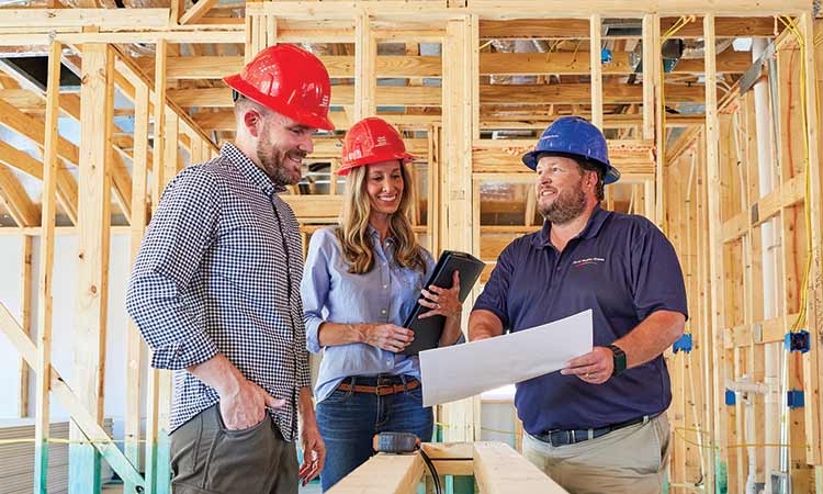 A David Weekley Homes Personal Builder showing two Homeowners floorplans while they stand in a home under construction, all three people are wearing hard hats