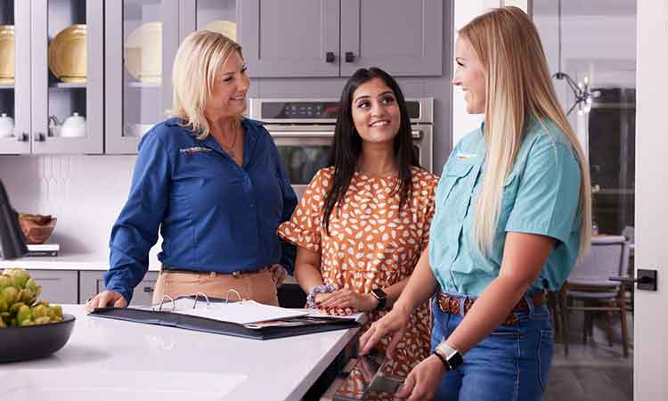 Two David Weekley Homes Team Members stand with a homeowner in a kitchen. They are reviewing a notebook and smiling