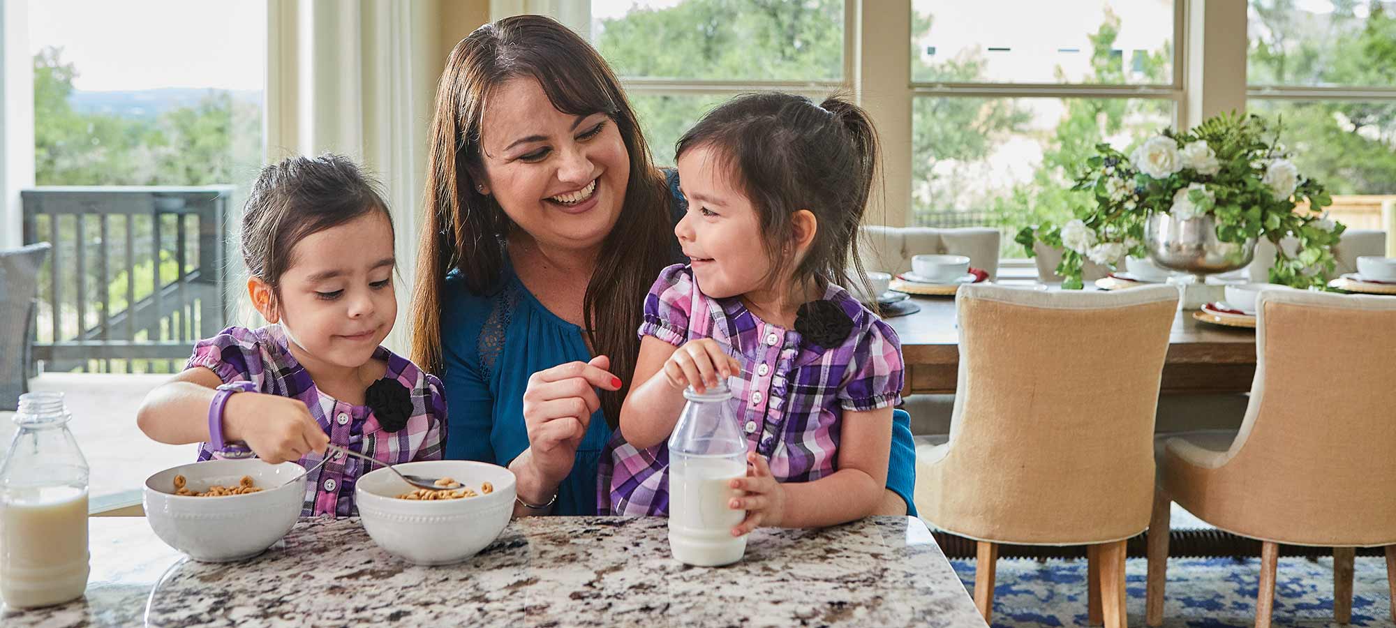 A woman sits at a kitchen counter with two children