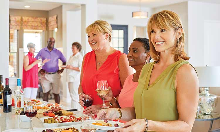 Three David Weekley Homes Homeowners standing at a kitchen counter holding plates of food and wine glasses