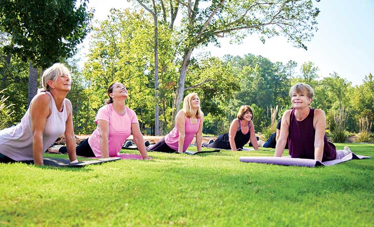 Five women outdoors on a grassy lawn doing yoga on yoga mats