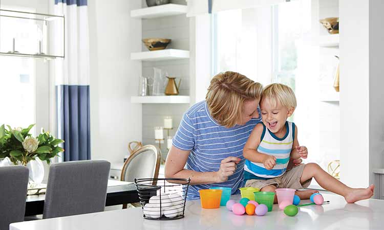 a woman and a child are sitting at a kitchen counter, there are bright, children's toys on the counter and the child is laughing