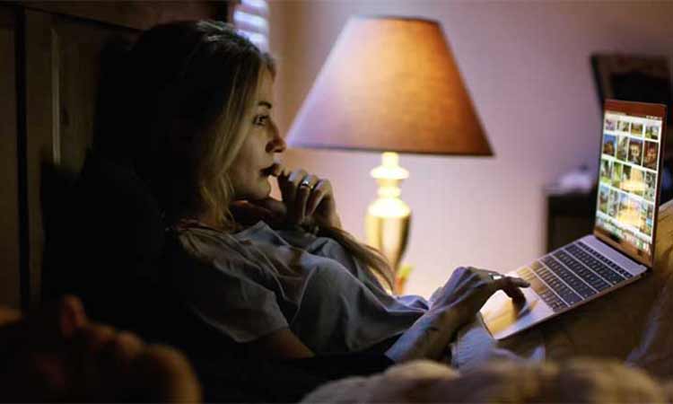 A woman sits up in bed while looking at a laptop