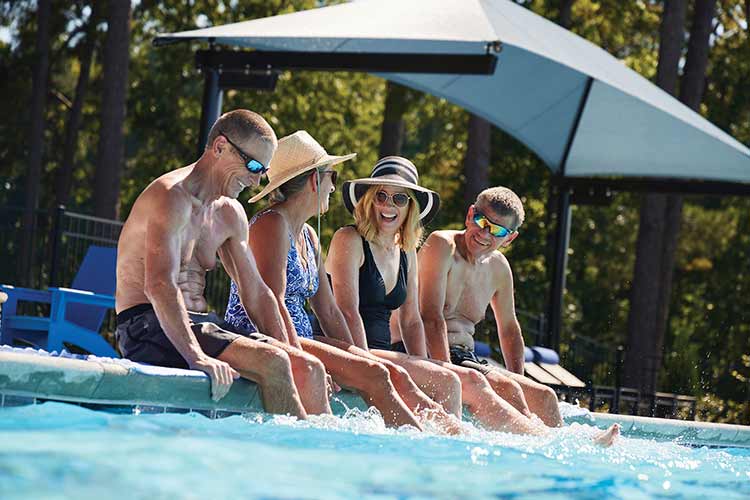 Four adults sitting on the edge of a pool and smiling