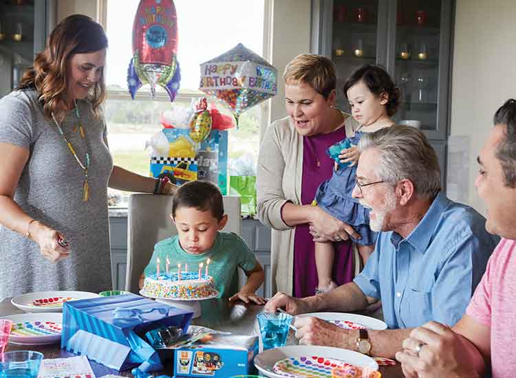 a family sitting a table, a young blows out candles on a birthday cake