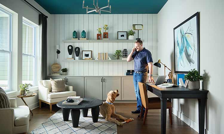 A homeowner standing in a study on the phone, there is a dog sitting on the floor in front of him