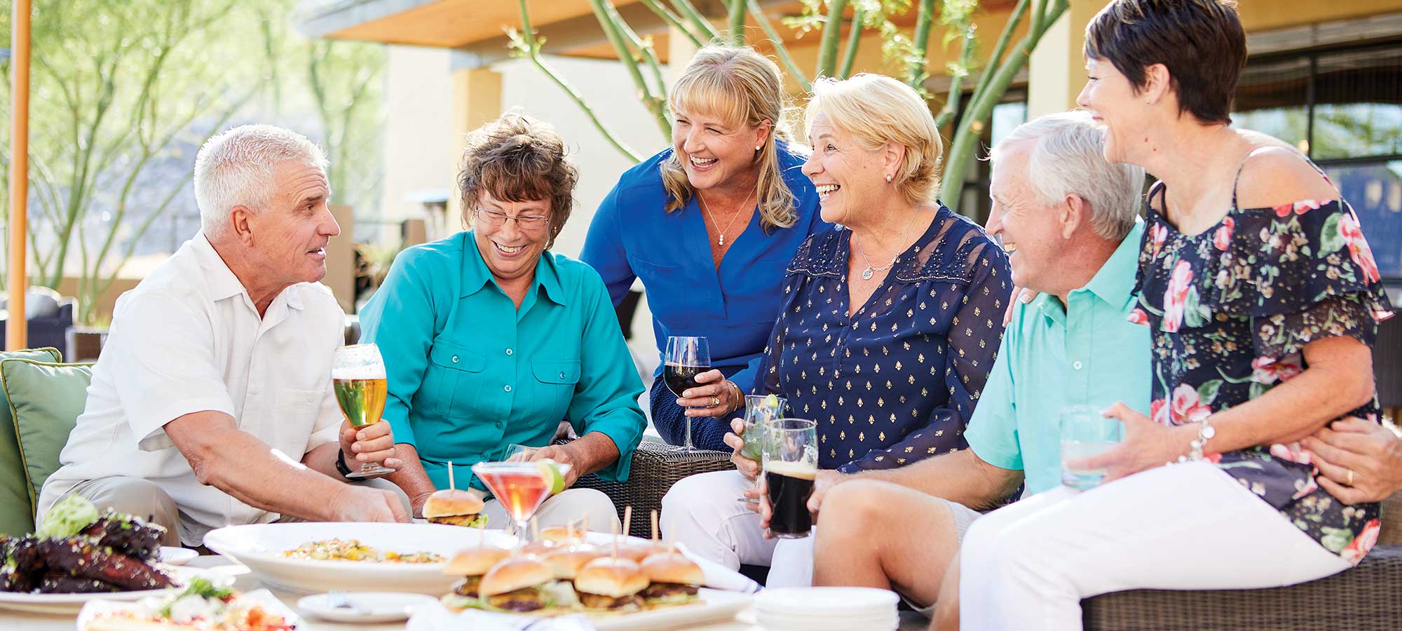 55+ people gathered around an outdoor table with food and drinks