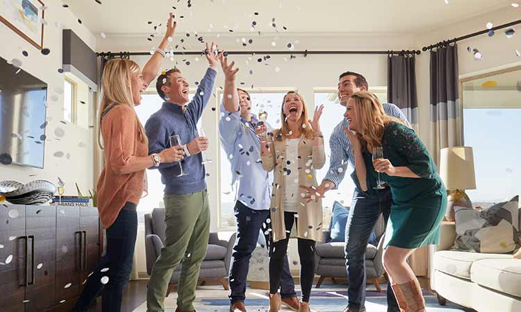 a group of people stand in a family room while holding glasses and throwing confetti in the air