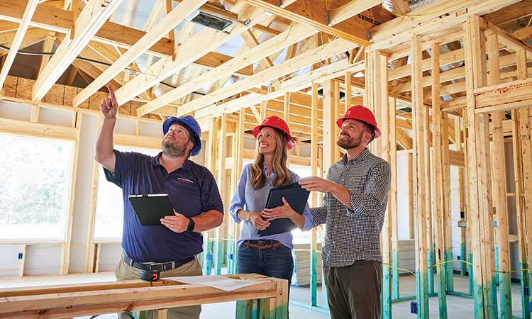 A David Weekley Homes Personal Builder walks through a home under construction with two people, all three people are wearing hard hats