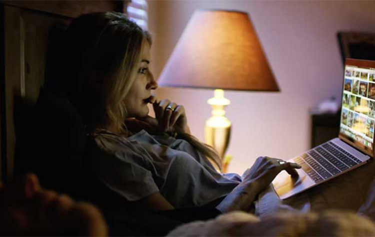 A woman sits in bed while looking at a laptop
