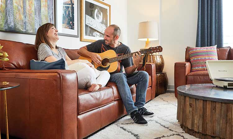A man and a woman sit on a couch, the man is playing the guitar