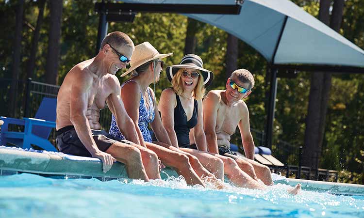 Four adults sitting on the edge of a pool, they are smiling and laughing
