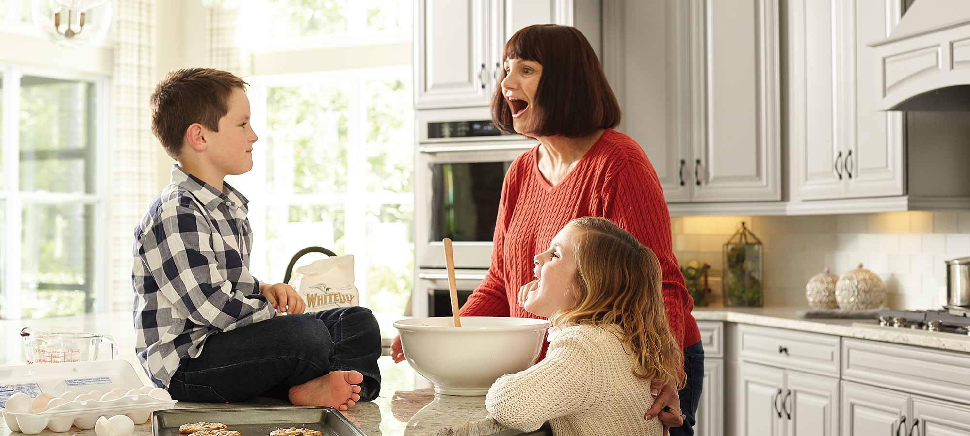 a woman bakes cookies with two children in a kitchen