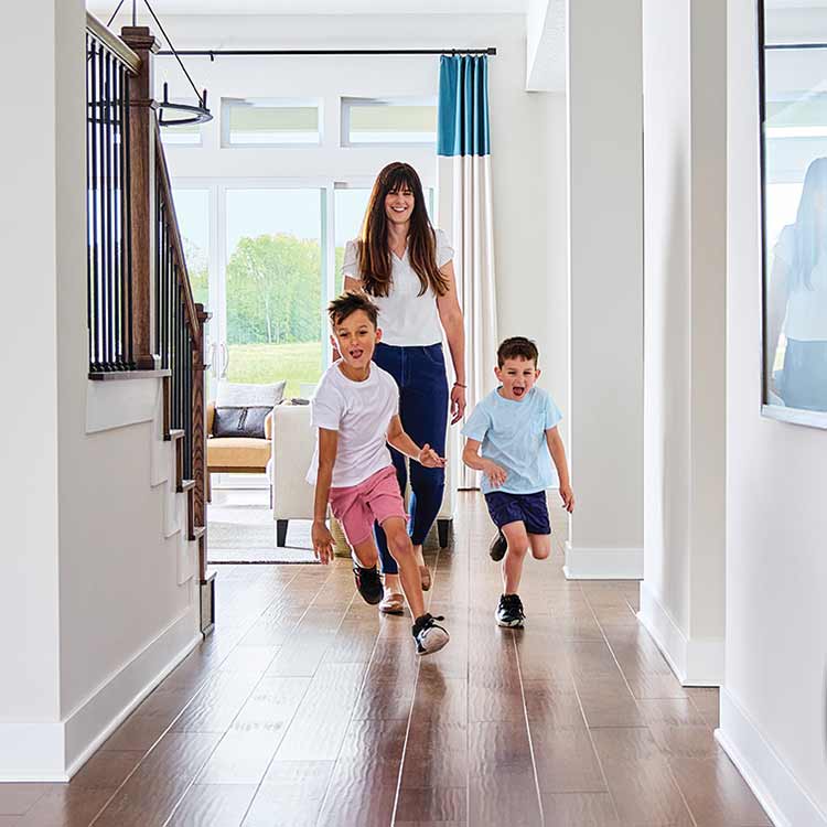 a woman smiles and walks through a home while two children are smiling and running in front of her